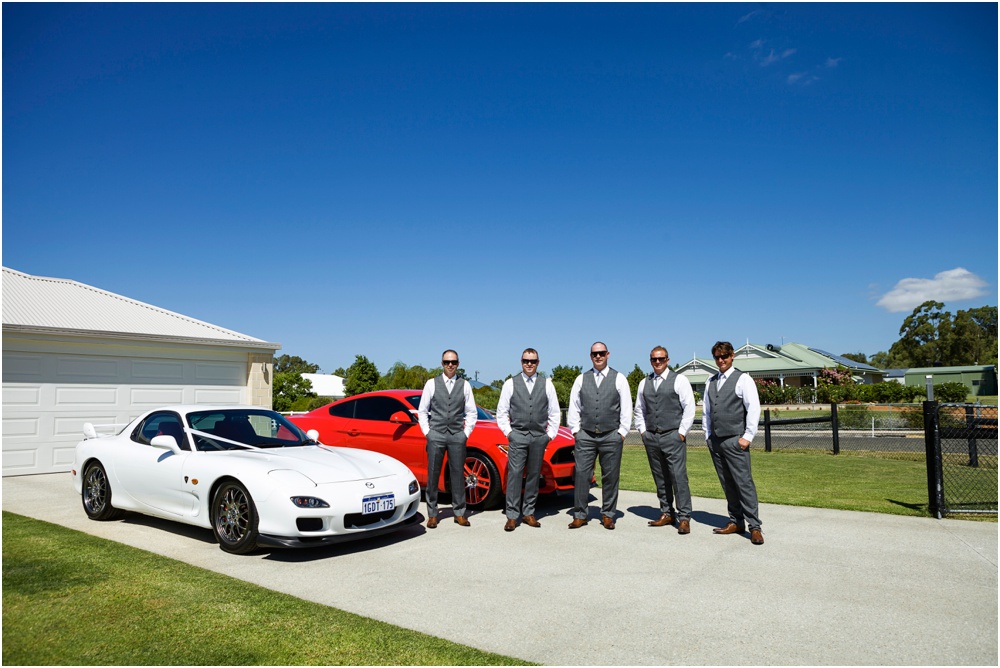 Groom with groomsmen stadnign with wedding cars
